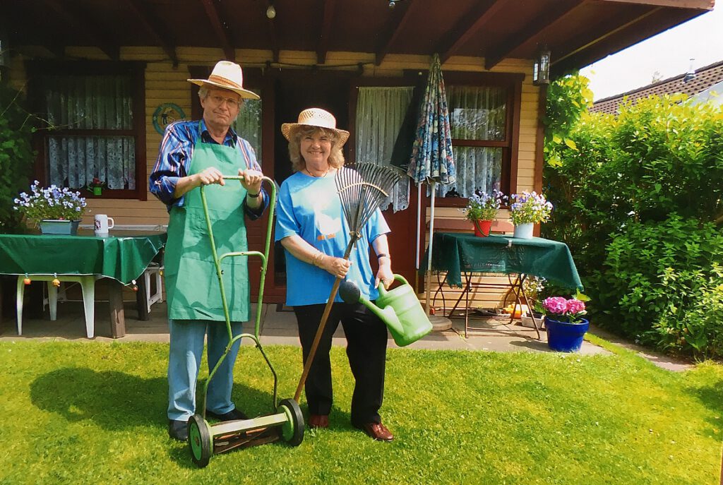Mann und Frau mit Rasenmäher und Gärtnerhut vor der Laube